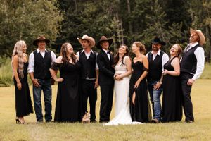 Wedding party in black attire with cowboy hats poses with bride and groom.