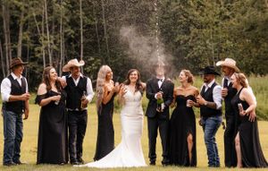 Wedding party celebrates outdoors with champagne spray, bridesmaids in black dresses and groomsmen in cowboy hats.
