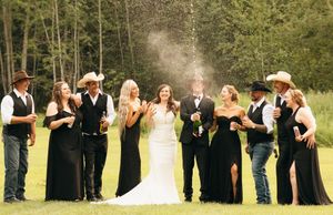 Wedding party laughs as champagne is sprayed during outdoor celebration on green grass.