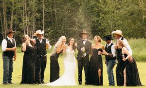 Bridal party pops champagne bottles in joyful celebration on a lush green lawn.