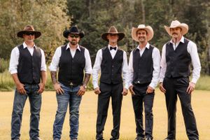 Five groomsmen in black vests, bow ties, and cowboy hats pose together on a grassy field.