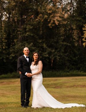 Bride and groom share a romantic portrait on a green lawn surrounded by tall autumn trees.