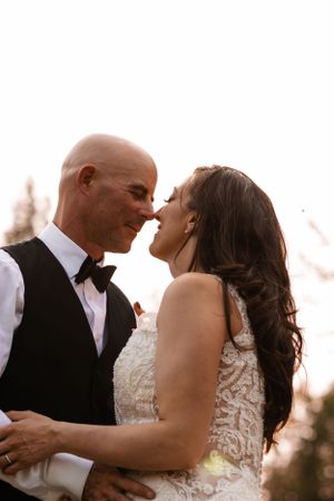 Close-up of bride and groom nearly kissing with warm backlit glow at outdoor wedding ceremony.