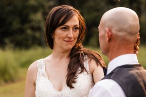 Close-up portrait of smiling bride with long brown hair looking at groom during outdoor wedding.