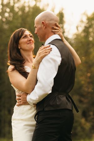 Bride and bald groom sharing a romantic dance embrace in golden sunset light outdoors.