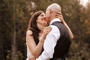 Bride and groom share a romantic moment, smiling and embracing outdoors with autumn trees in background.