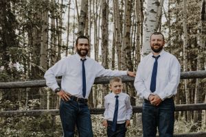 Three males in white shirts and navy ties pose by a rustic wooden fence in a birch forest.