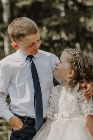 Young boy in white shirt and tie smiling at little girl in flower girl dress.