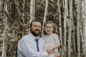 Father holding young daughter smiling in birch tree forest wedding photo.