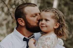 Father kissing young daughter on cheek during outdoor wedding photo session.