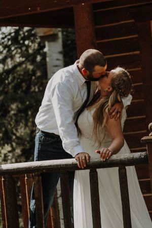 Bride and groom share a tender kiss on a rustic wooden cabin porch.