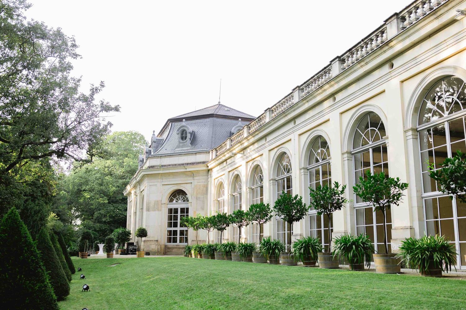 Panoramic view of an elegant historic building with white arched windows and ornate architectural details in a garden setting.