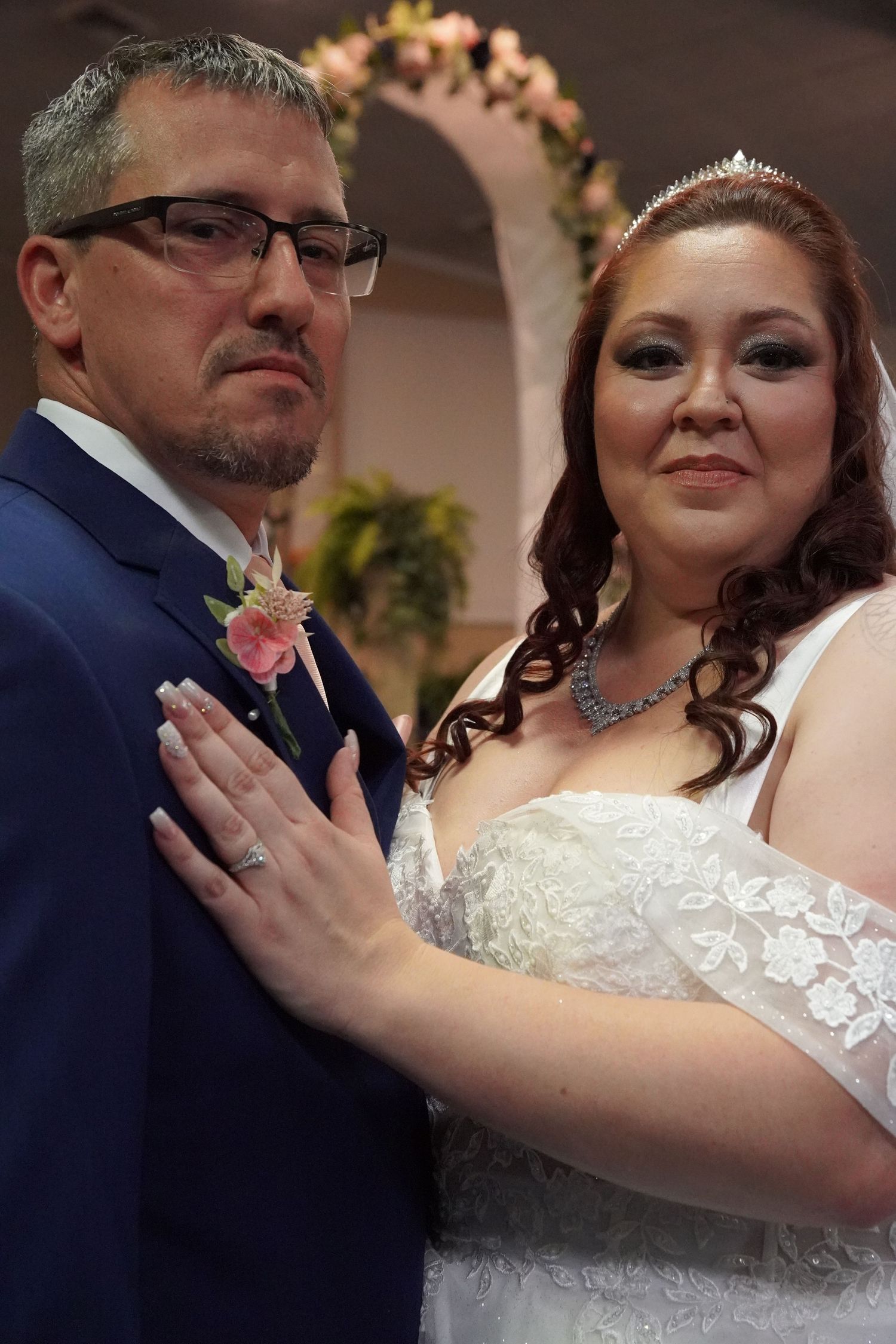 Bride putting hand on grooms chest smiling at the camera at their wedding.