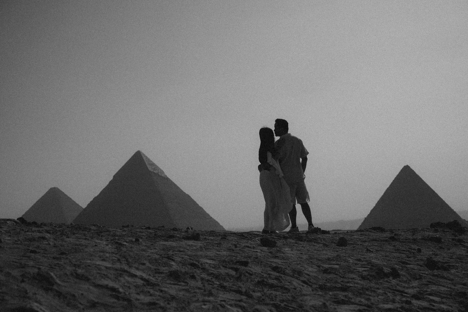 Romantic embrace captured against the iconic pyramids of Giza and cloudy desert sky.