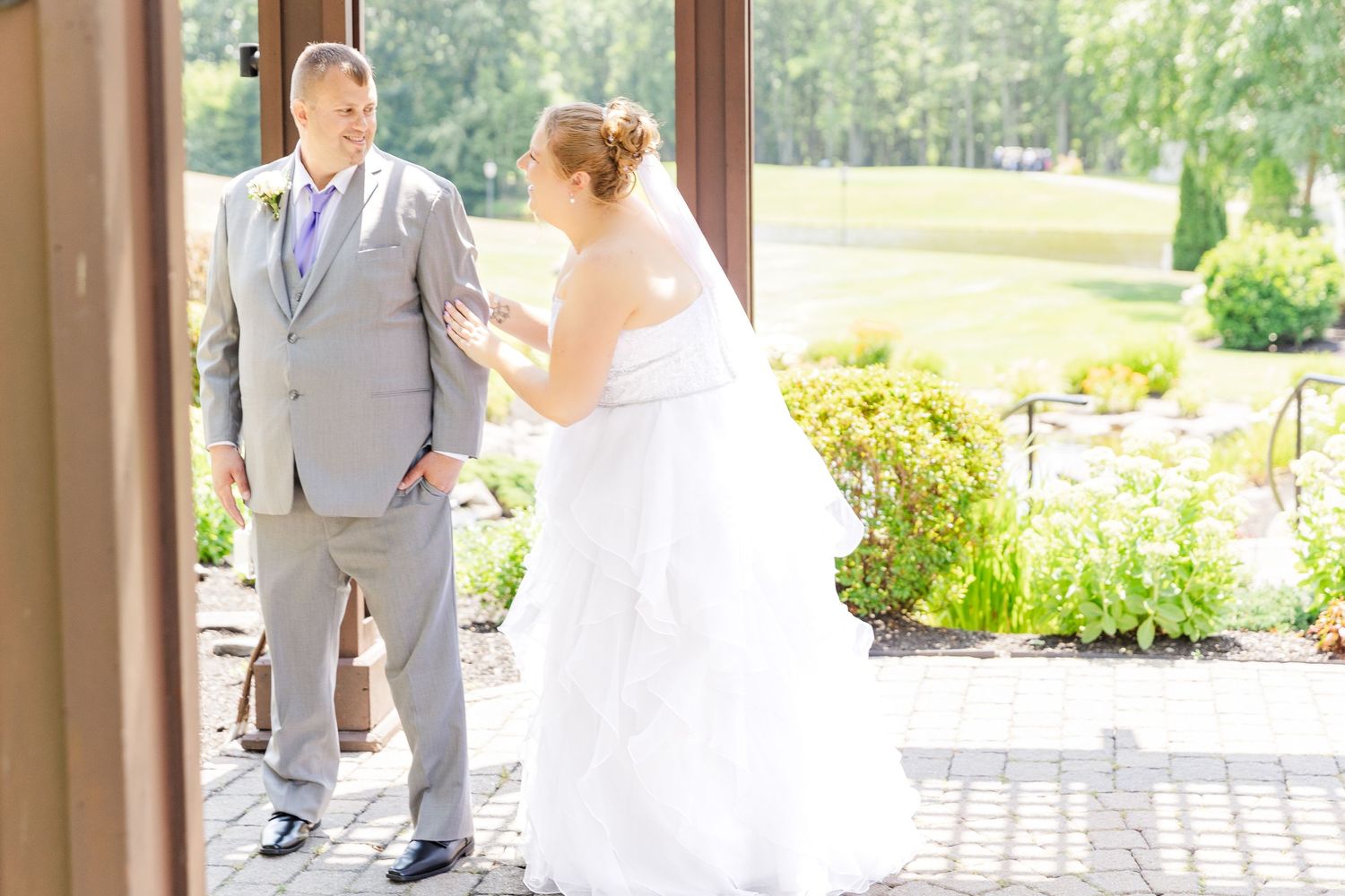 Wedding couple has their first look on an elegant covered patio with landscaped gardens in background.