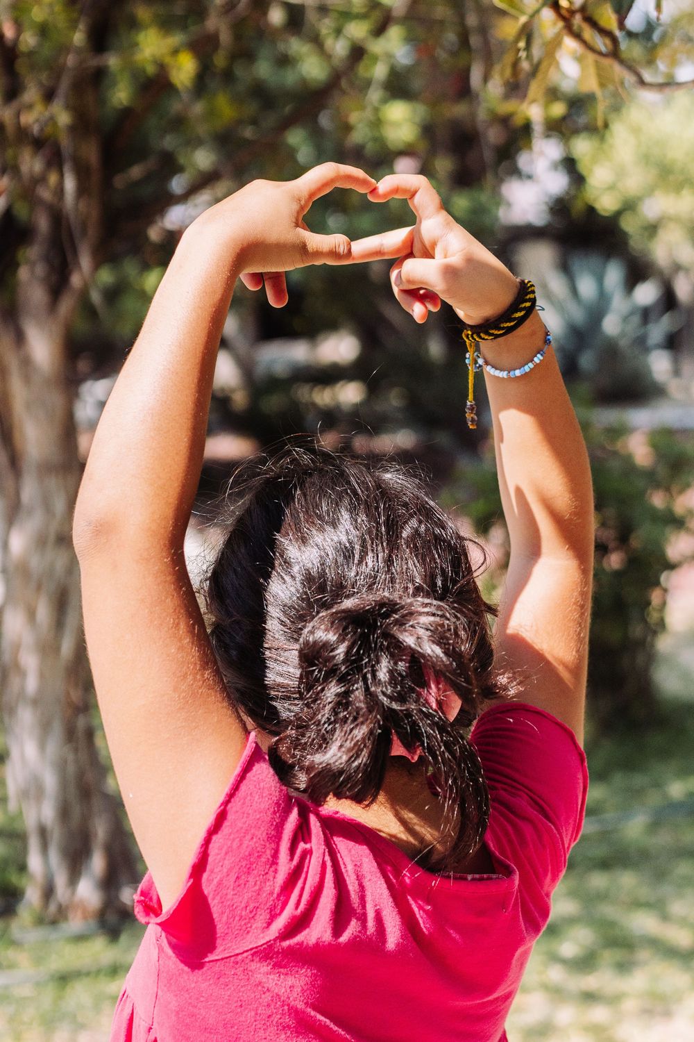 Person in red shirt stretching arms upward outdoors with trees in background.