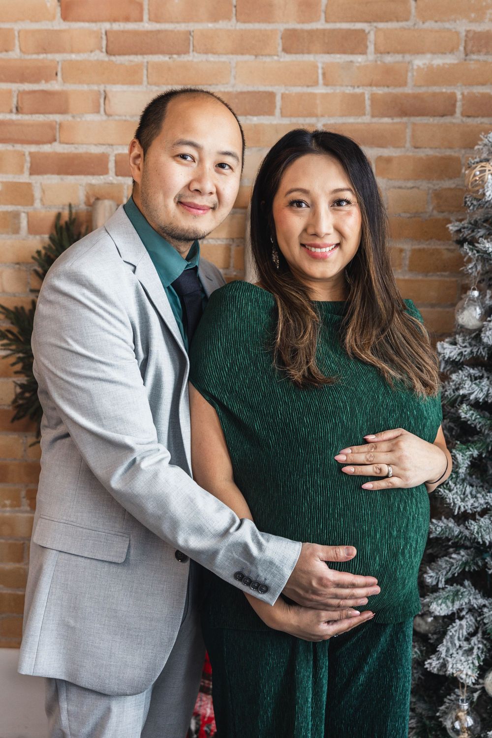 A couple in festive attire poses together for holiday photos with decorated trees in the background.