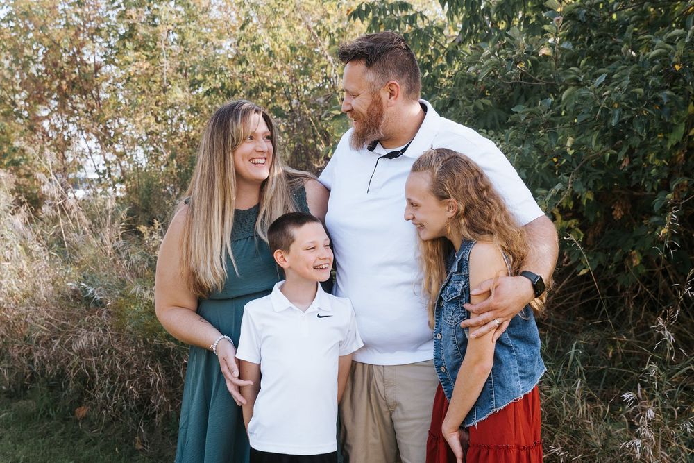 A family group shares a playful moment outdoors in casual white and denim clothing.