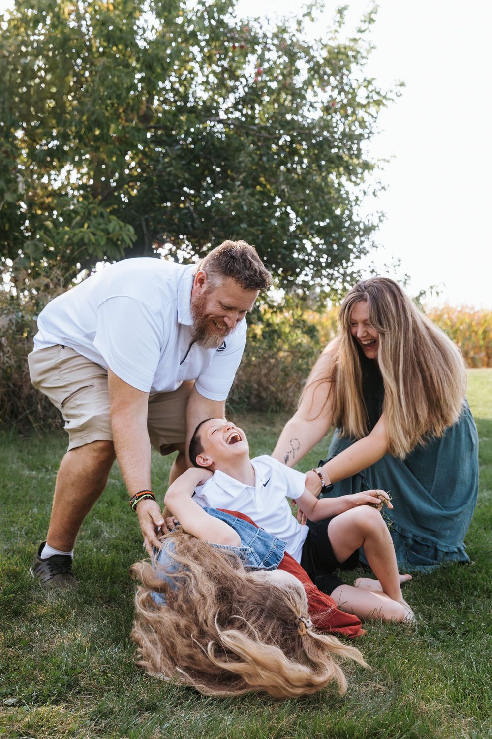 A family plays and laughs together while lying on grass during an outdoor photo session.