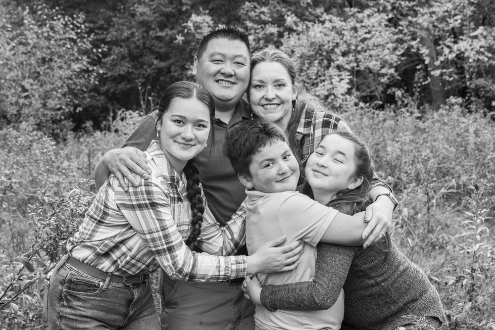 A group shares joyful embraces and laughter in a black and white outdoor photo.