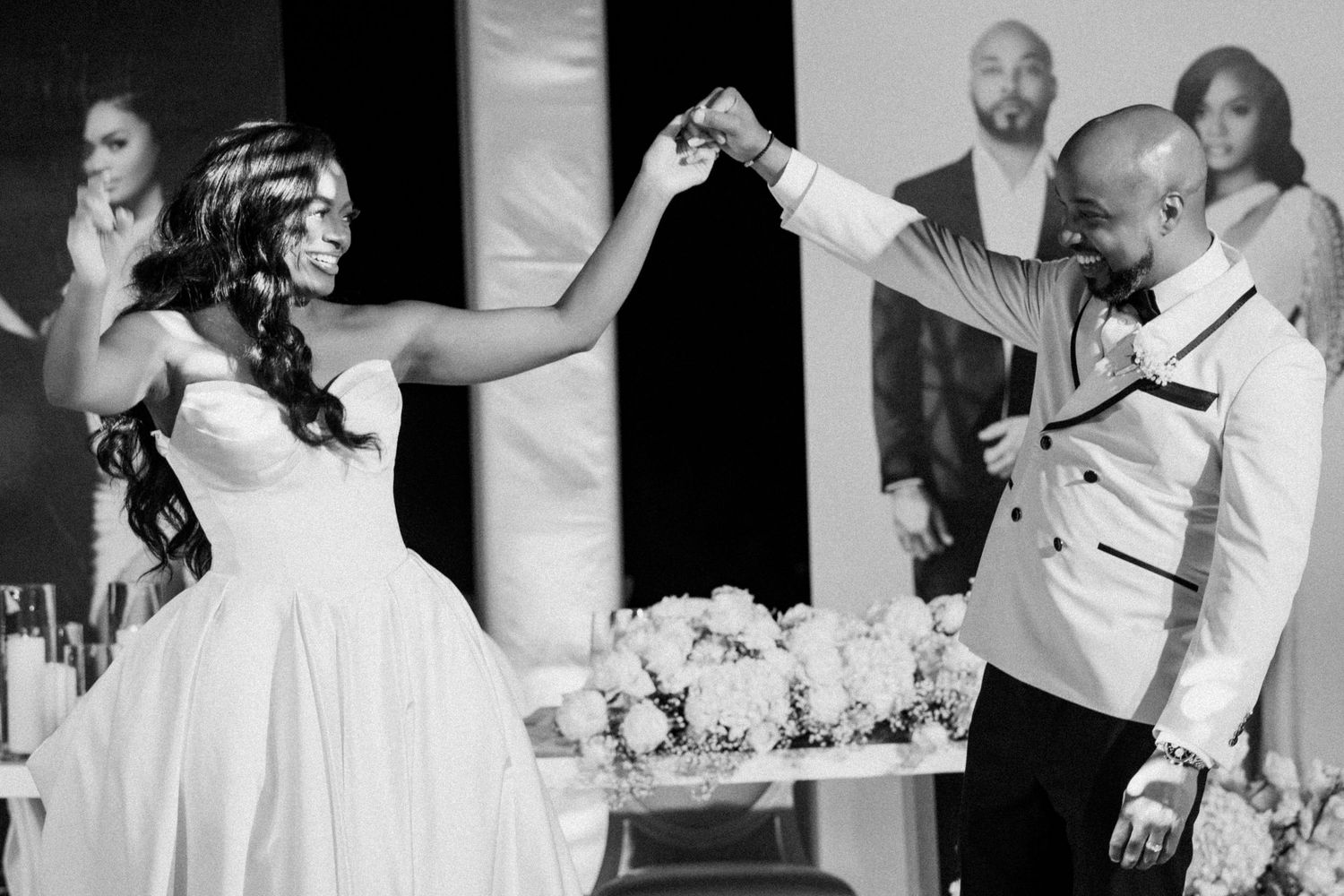 Black and white photo of a bride and groom dancing joyfully at their wedding reception.