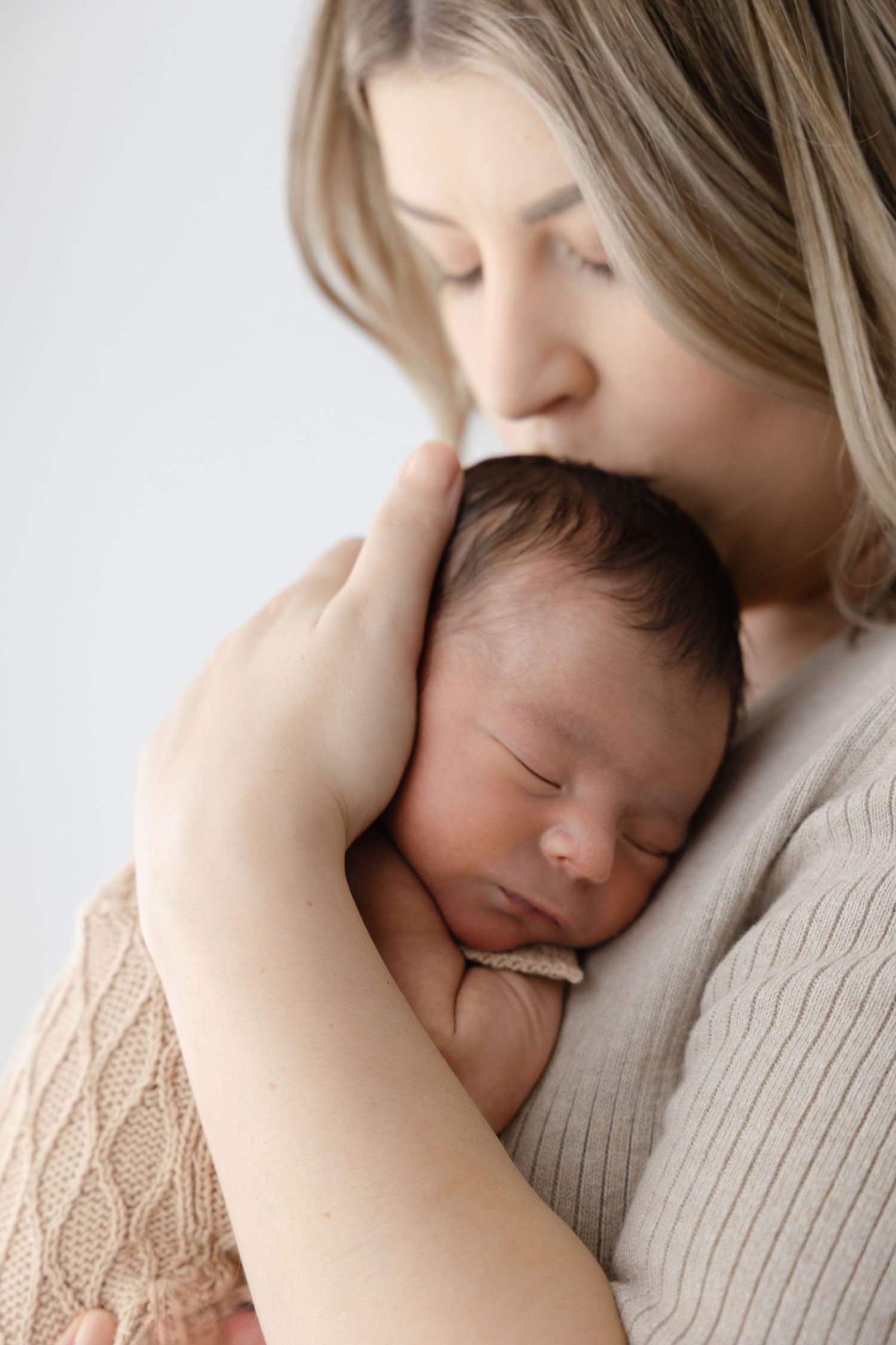 Tender close-up portrait of sleeping newborn being cradled against mother's chest.