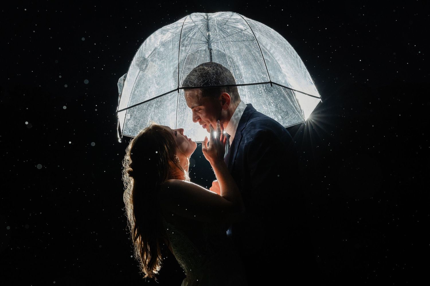 Romantic nighttime portrait of couple kissing under clear umbrella in the rain.