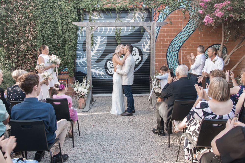 Wedding ceremony taking place in a courtyard with ivy-covered walls and decorative pergola.