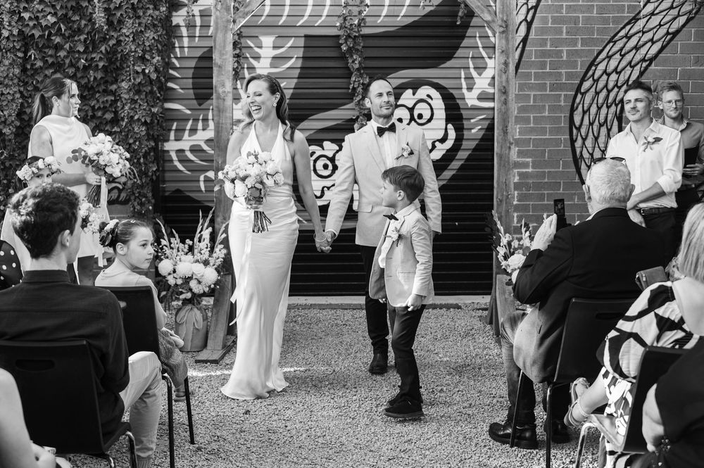 Black and white photo of a wedding ceremony with guests seated and a couple walking down brick steps.