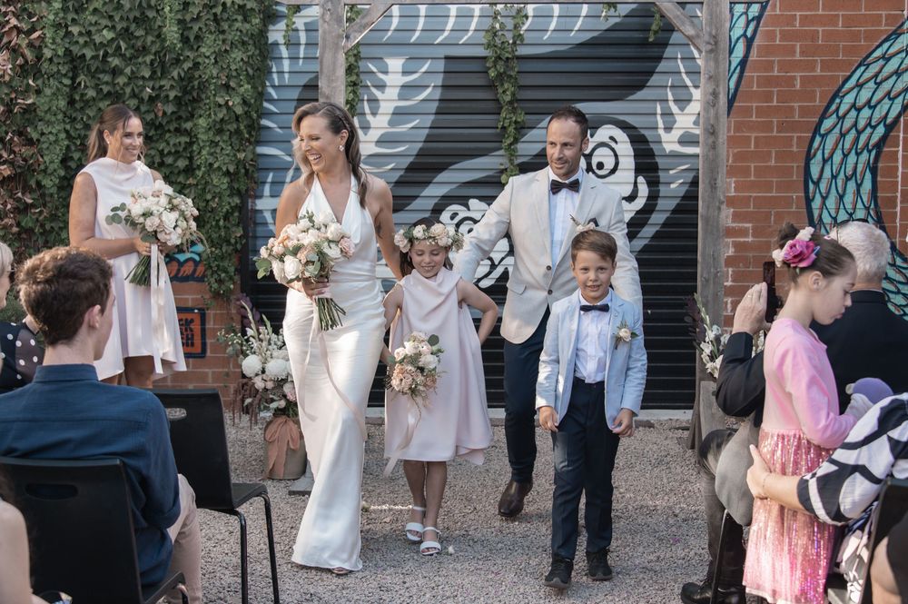 Wedding celebration scene outdoors with guests and decorative brick wall background.