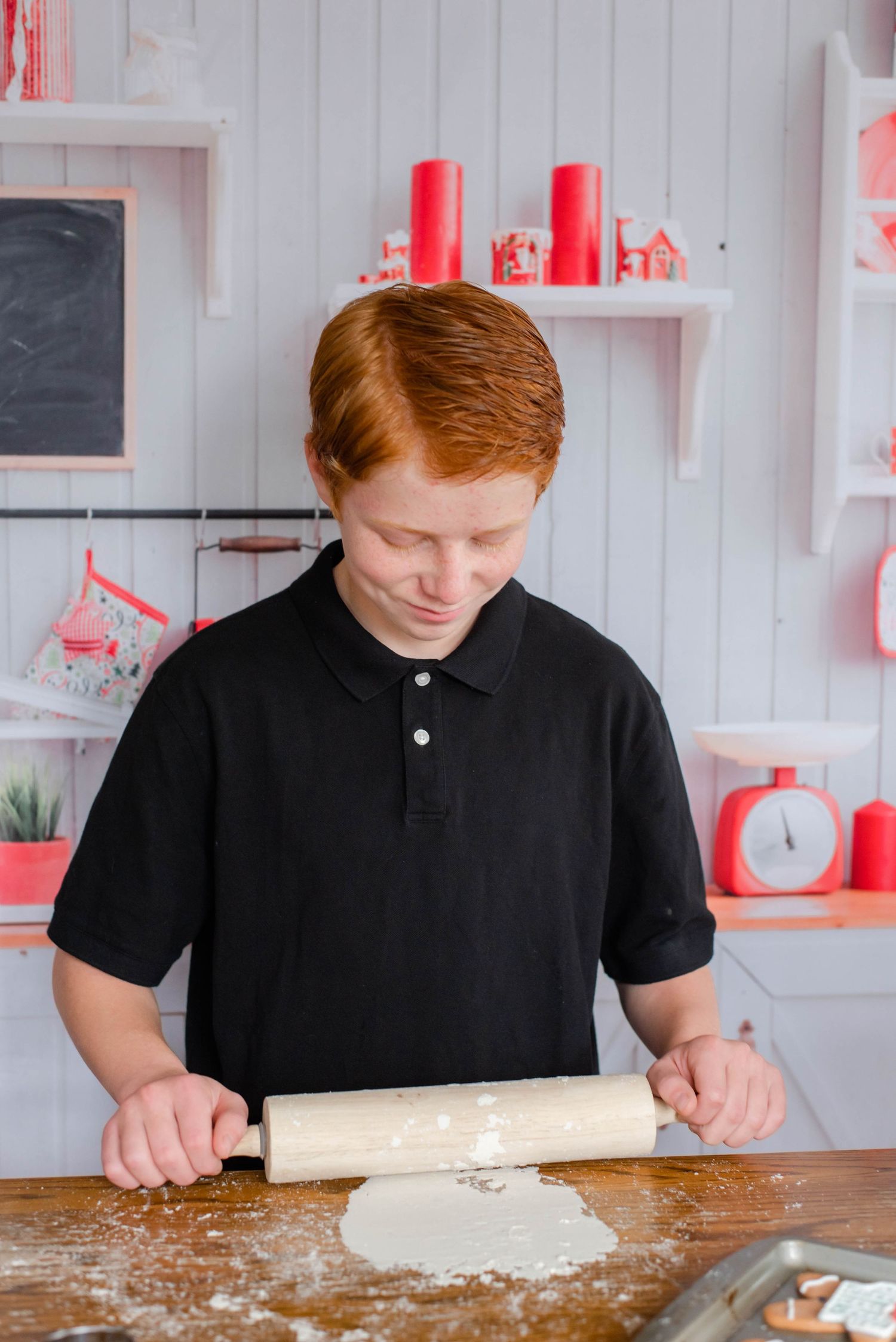 Person in black polo shirt rolling out dough on wooden surface.