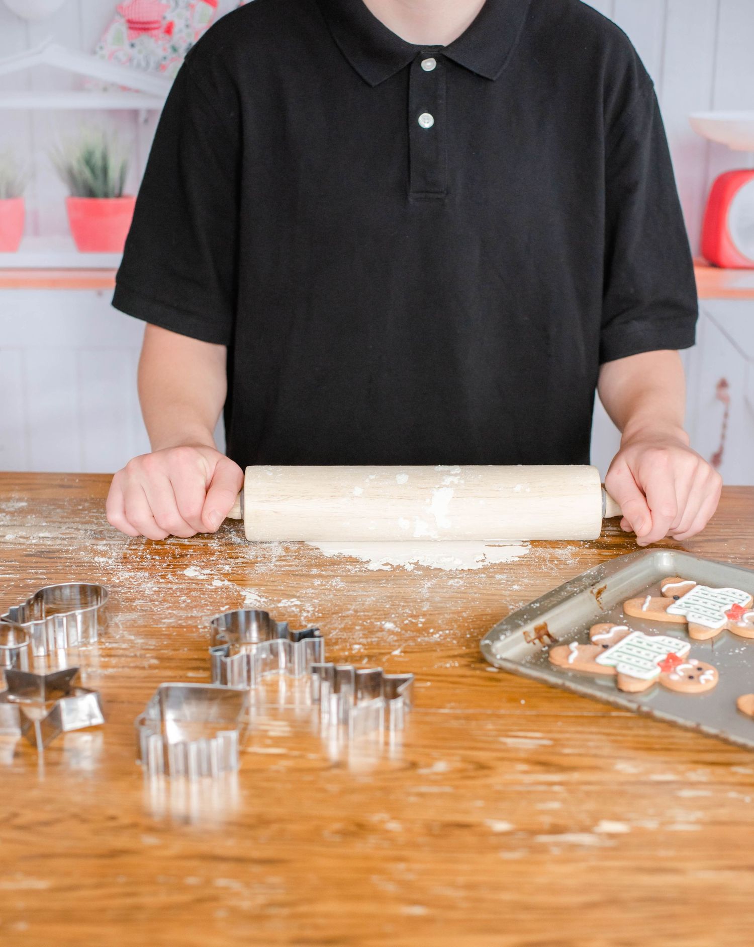 Baker working with dough and cookie cutters on wooden countertop.