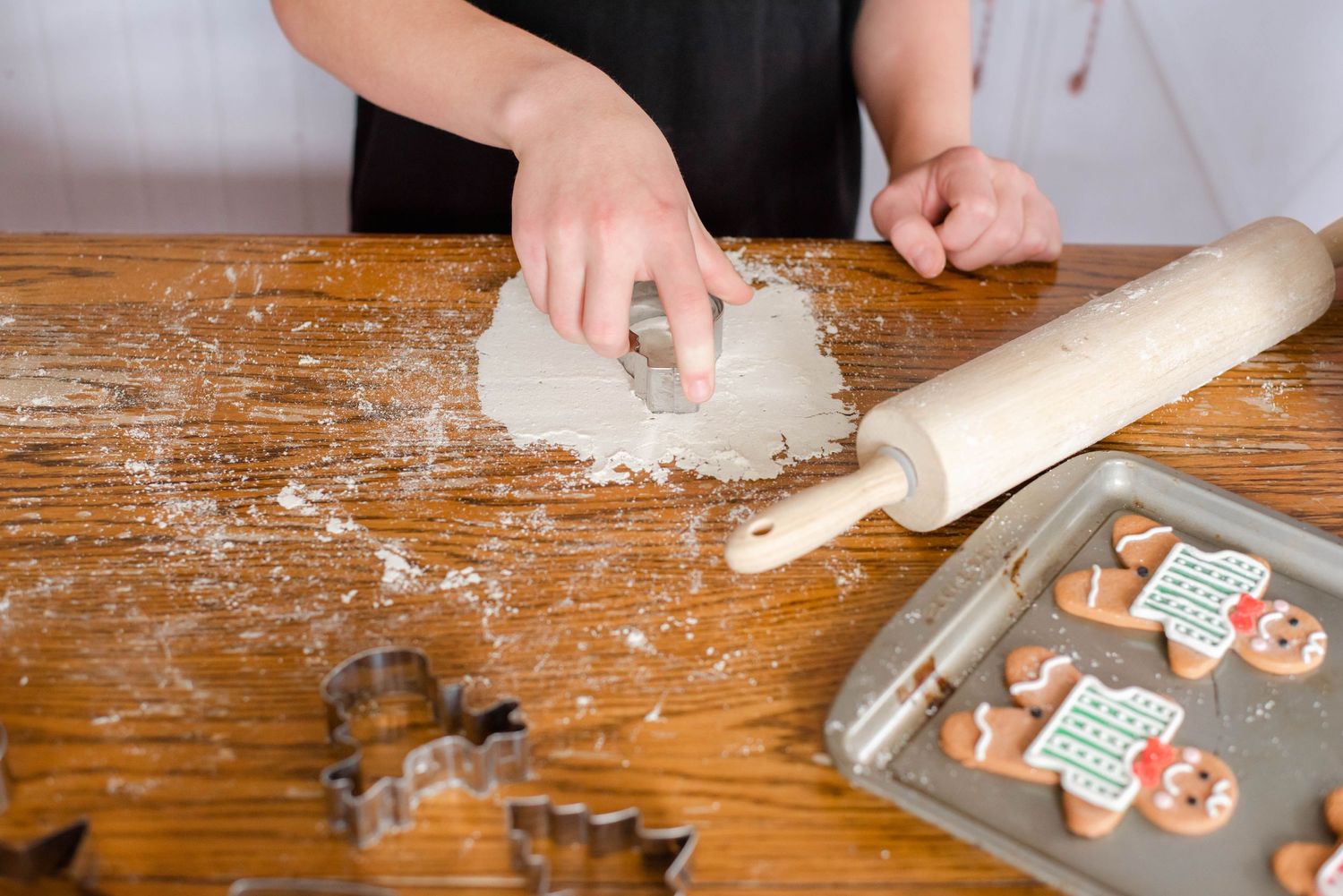 Rolling out cookie dough on a rustic wooden table with cookie cutters nearby.