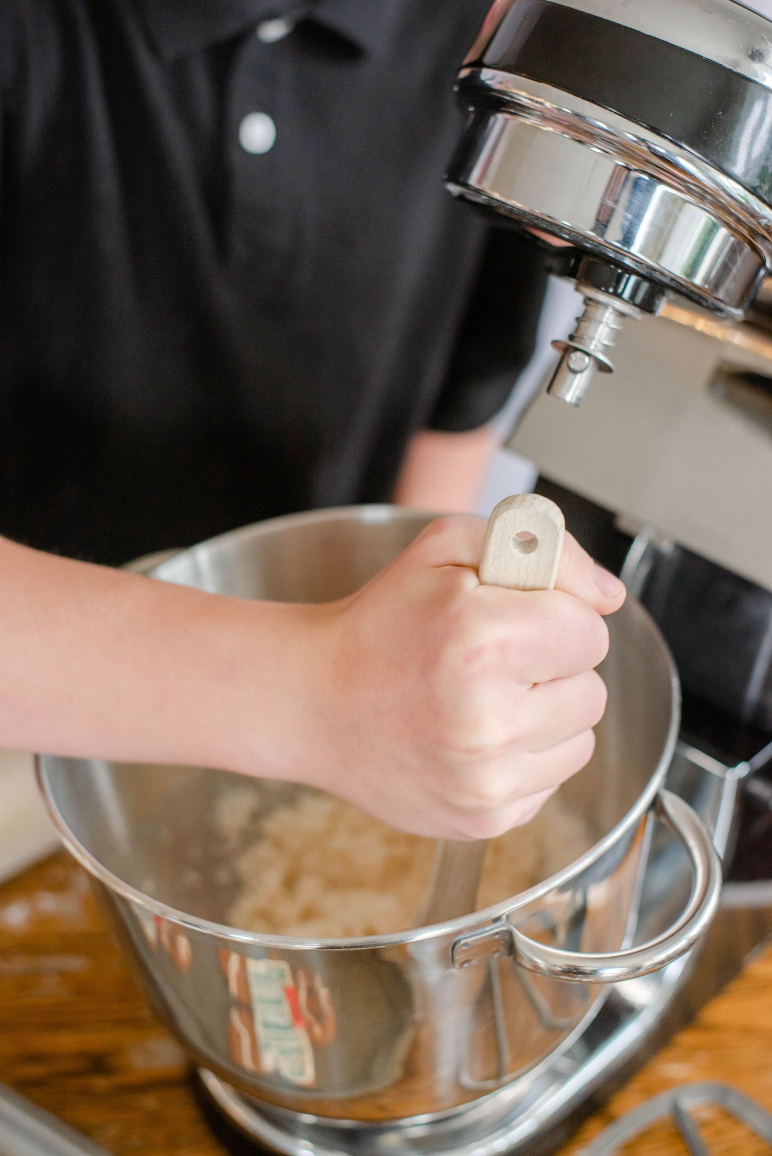 Close-up view of hands operating a silver stand mixer while baking.
