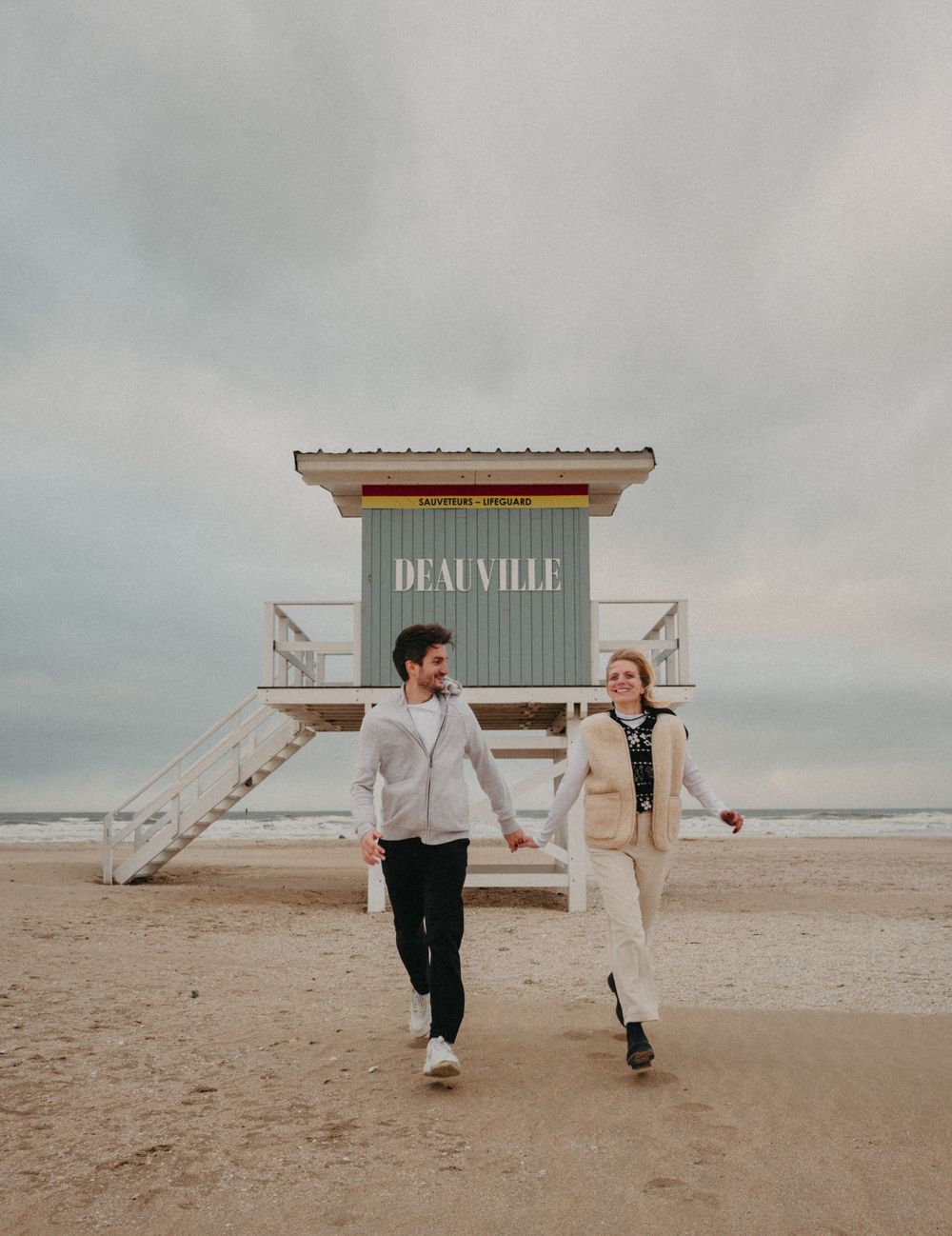 Engagement shoot at the beach with couple walking hand in hand during destination shoot in Deauville, France.