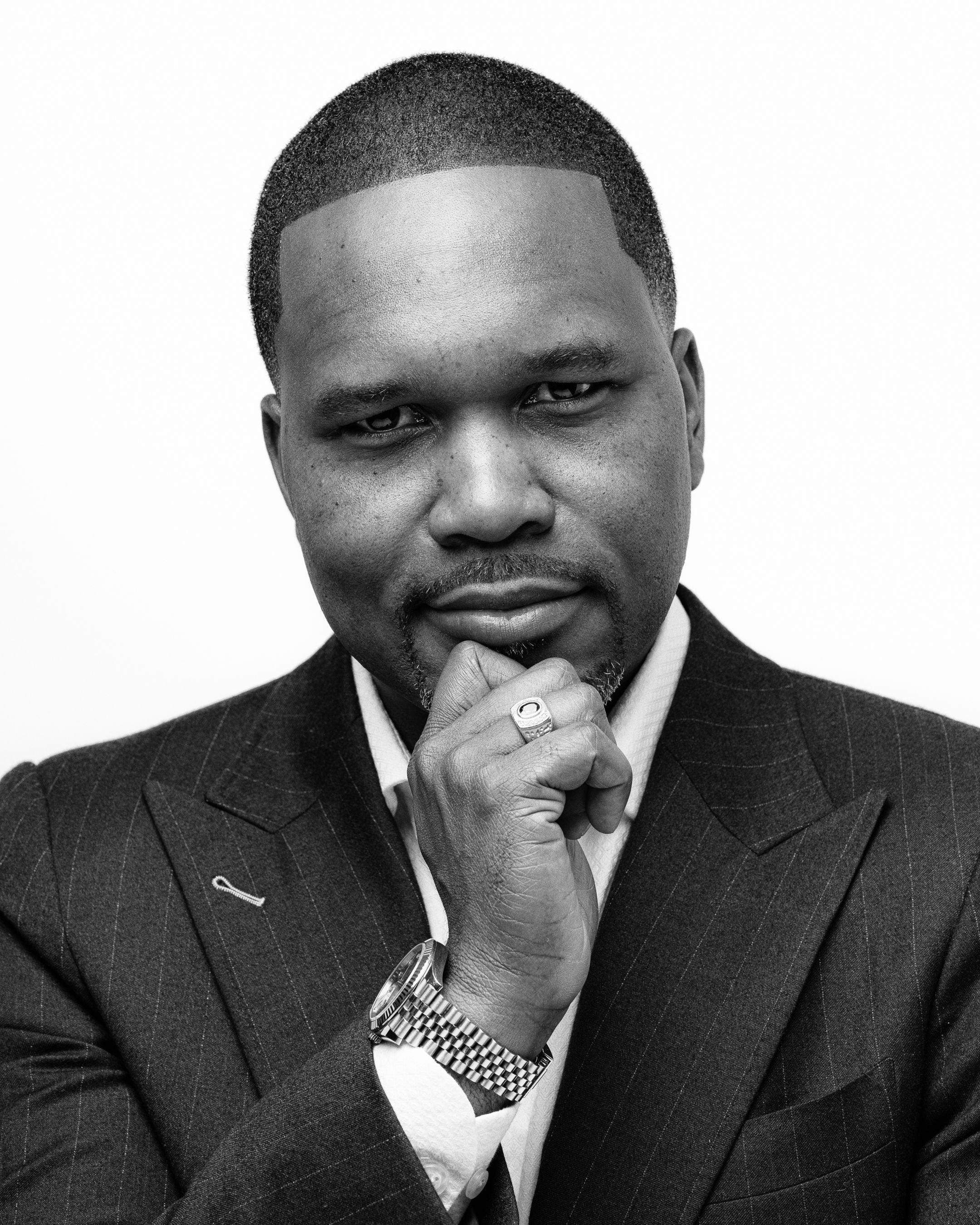 Professional black and white portrait of a person in a dark pinstriped suit with a thoughtful pose and hand on chin.