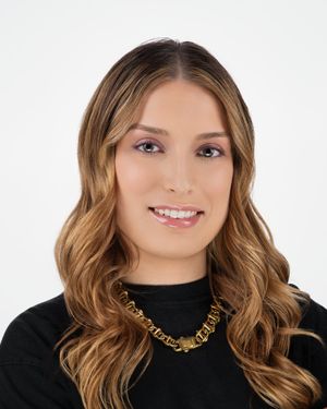Studio portrait of a smiling person with wavy blonde highlights wearing a black sweater and gold chain necklace.