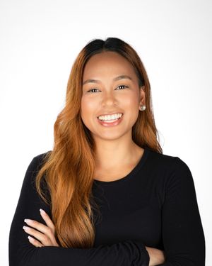 Professional studio portrait of someone with long caramel-colored hair wearing a black long sleeve top against white background.