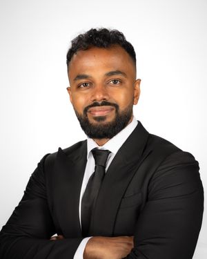 Professional headshot of a professionally dressed person in a black suit and tie against a white background.