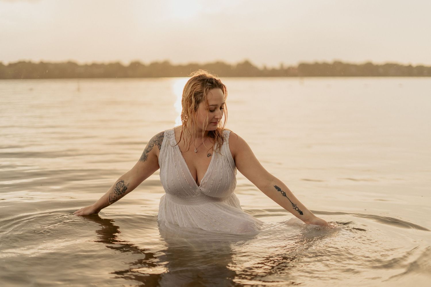 Ethereal sunset photo of person in flowing dress wading in serene lake waters.
