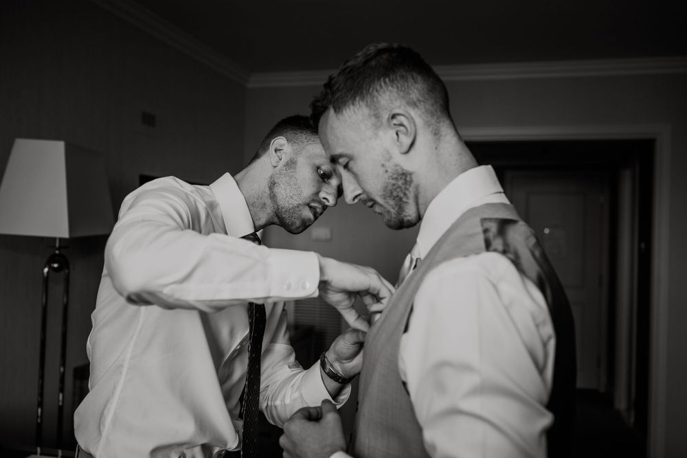 Two people in white dress shirts and vests sharing a candid moment in black and white.