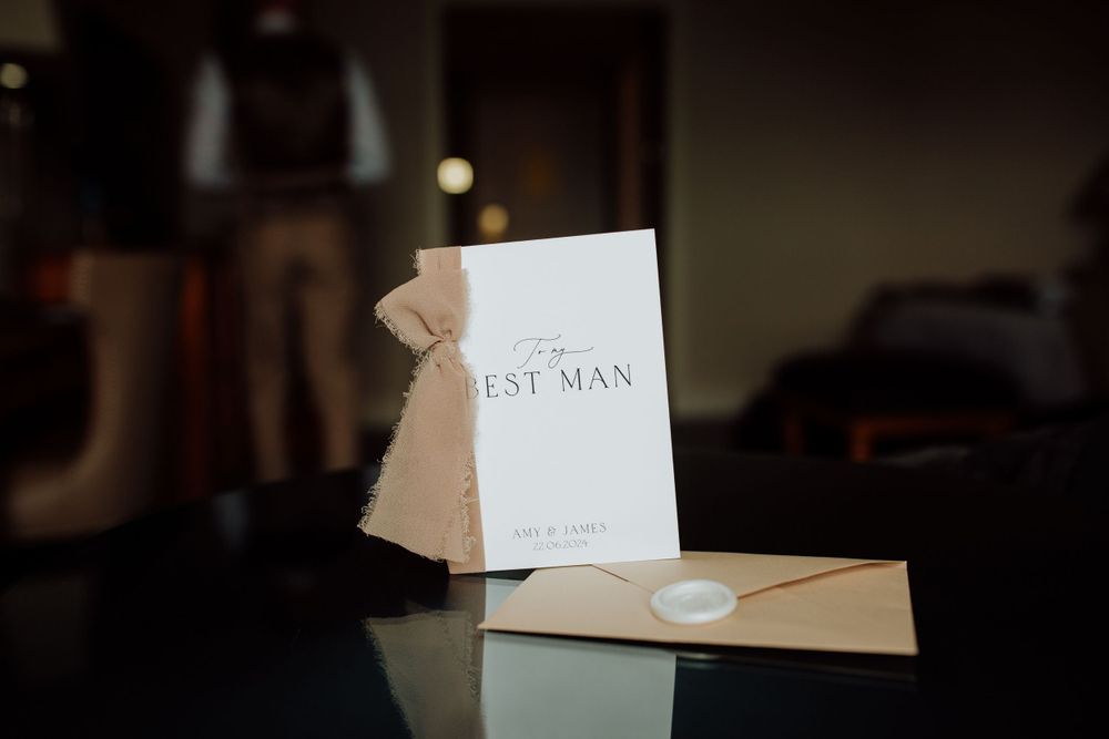 Best man card and envelope sitting on reflective surface in moody lighting.
