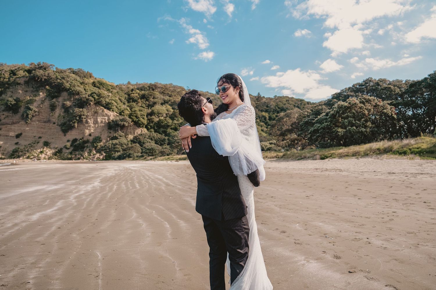 A couple holding hands while walking along the shoreline in casual attire.