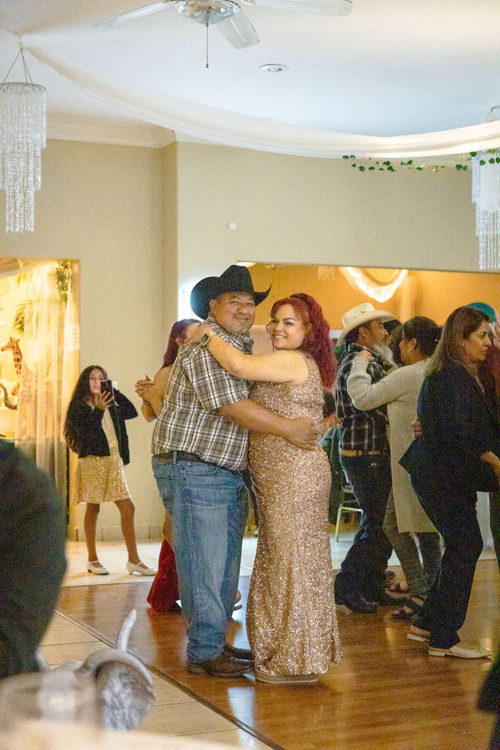 Guests dancing together at a formal event in a room decorated with white drapes and crystal chandeliers.