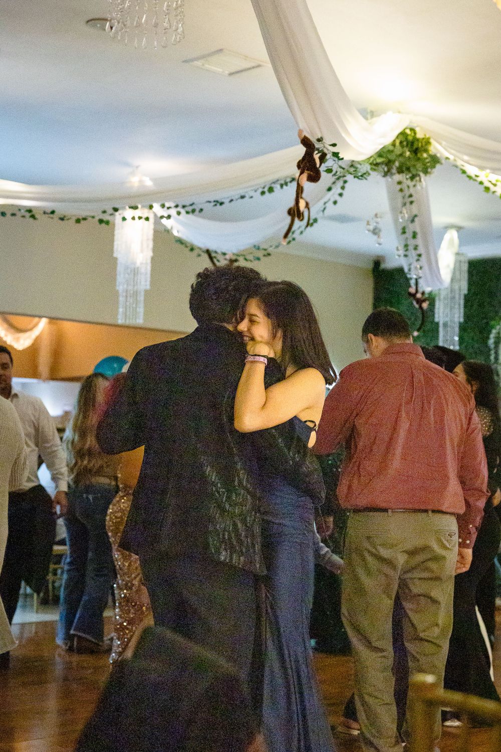 Couples dancing under white fabric draping and crystal chandeliers at an indoor event.
