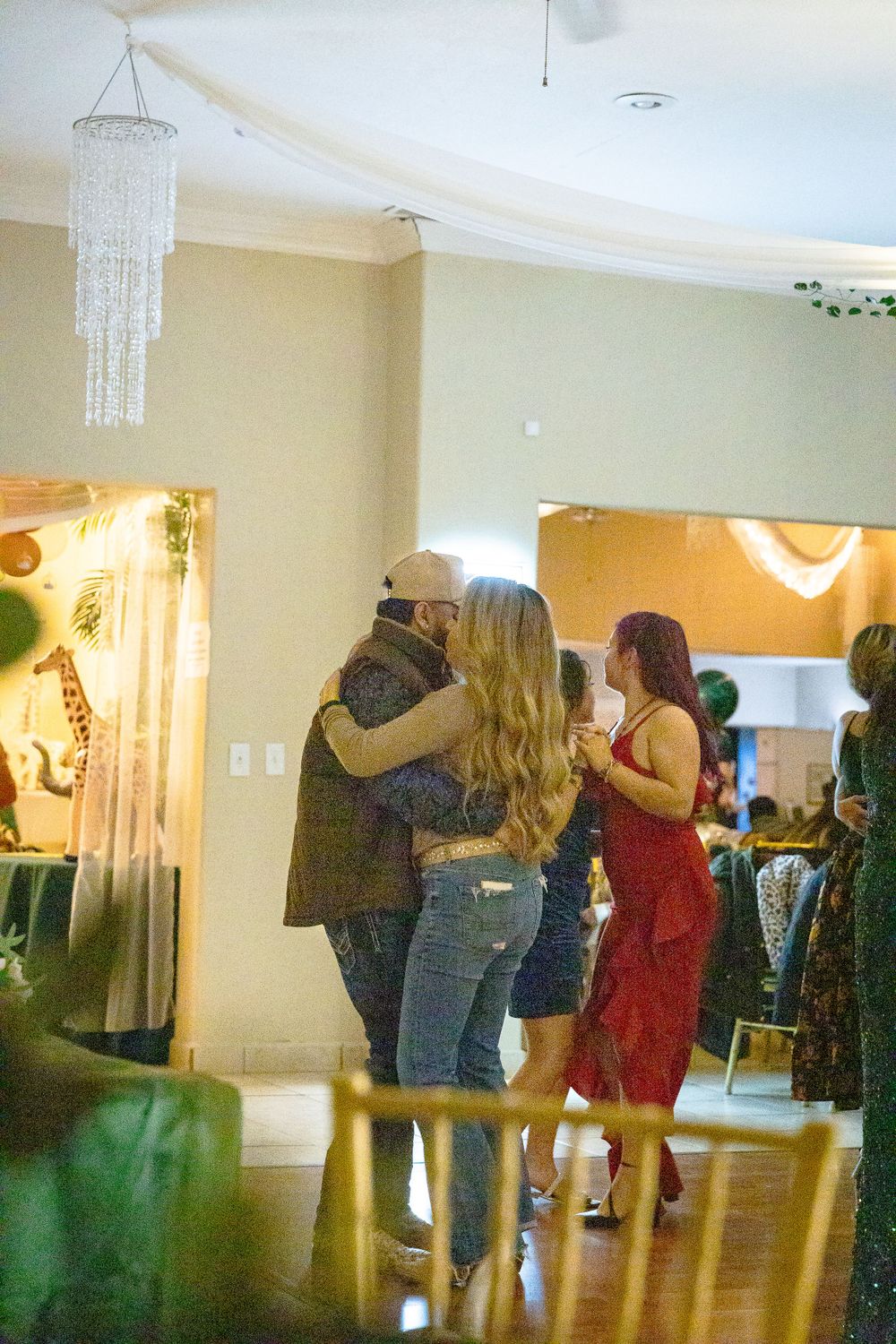 People dancing together at a celebration in a decorated room with hanging crystal chandeliers.
