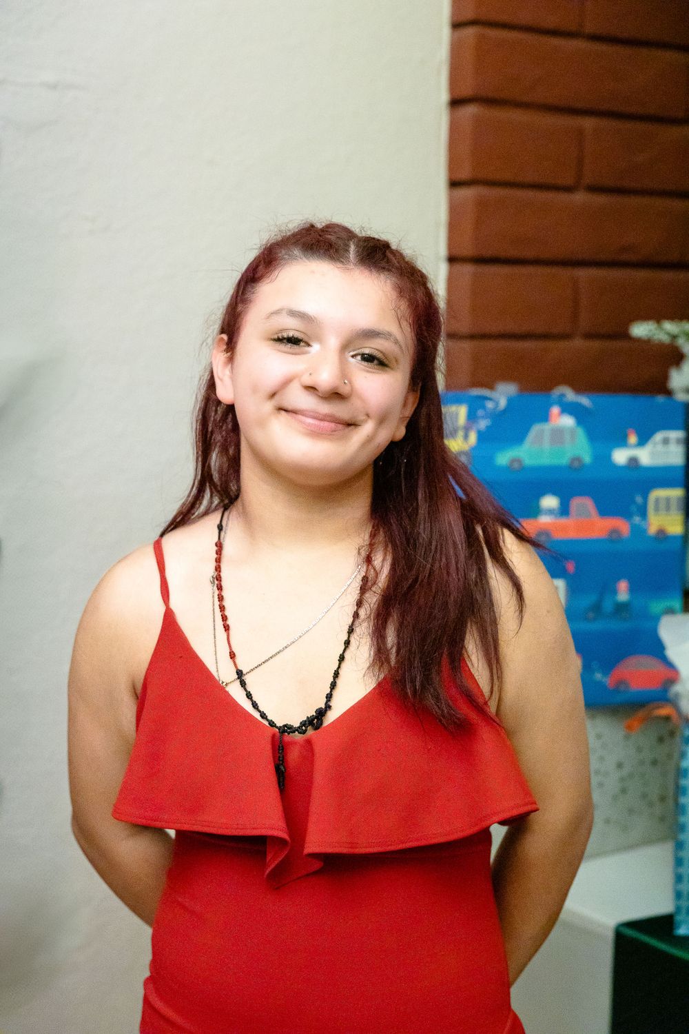 Guest in a red ruffled dress smiles at a party with decorative backdrop.
