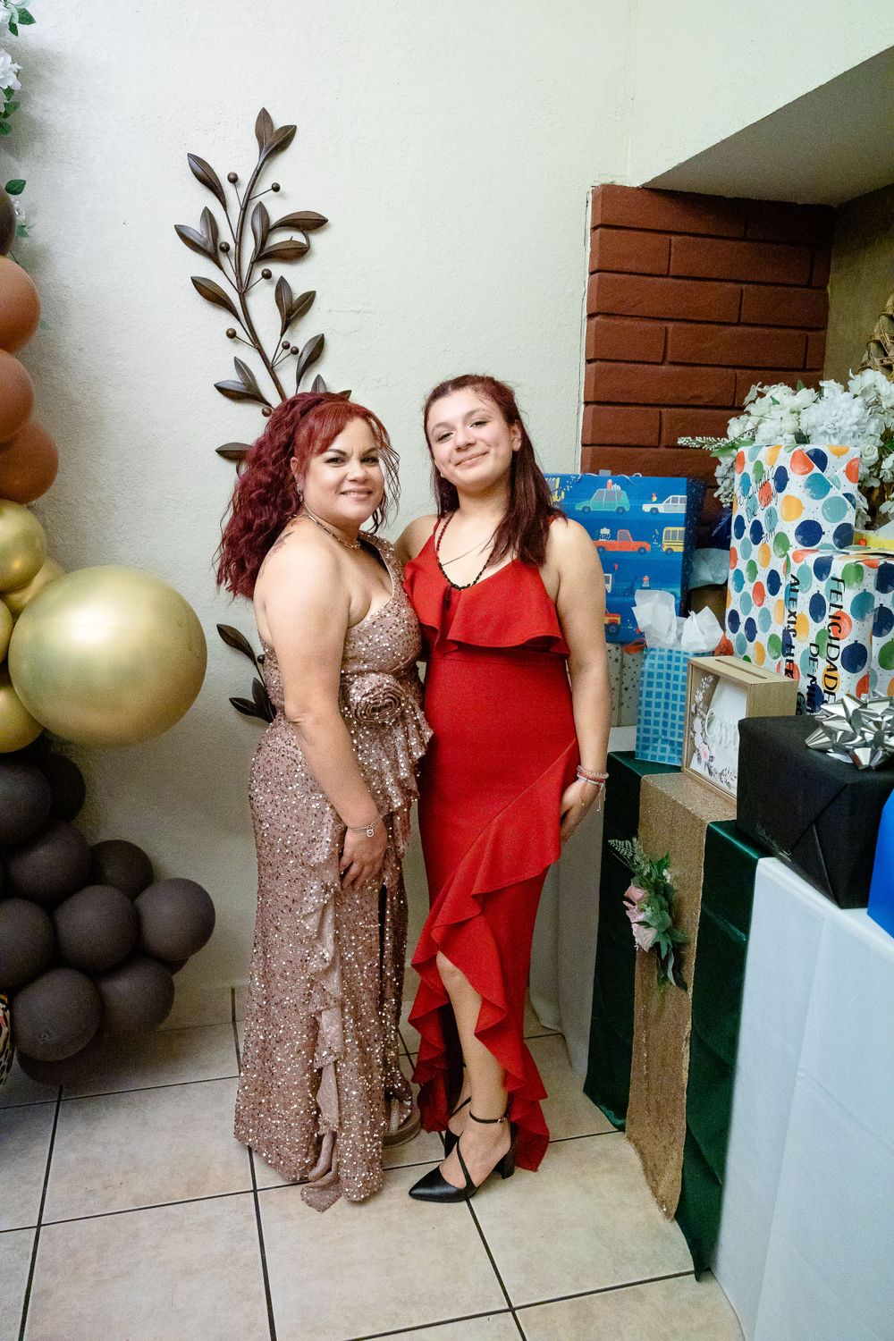 Two guests in formal dresses pose by balloon decorations and gift tables at a party.