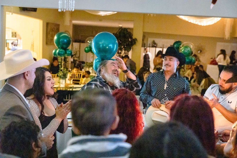 Party guests gathered in a decorated venue with teal balloons hanging from the ceiling.
