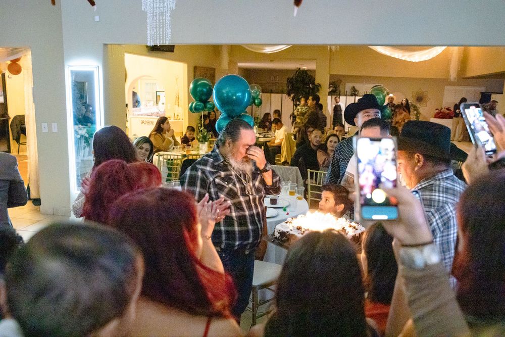 Crowd of people celebrating at an indoor event with teal balloons and decorative lighting.